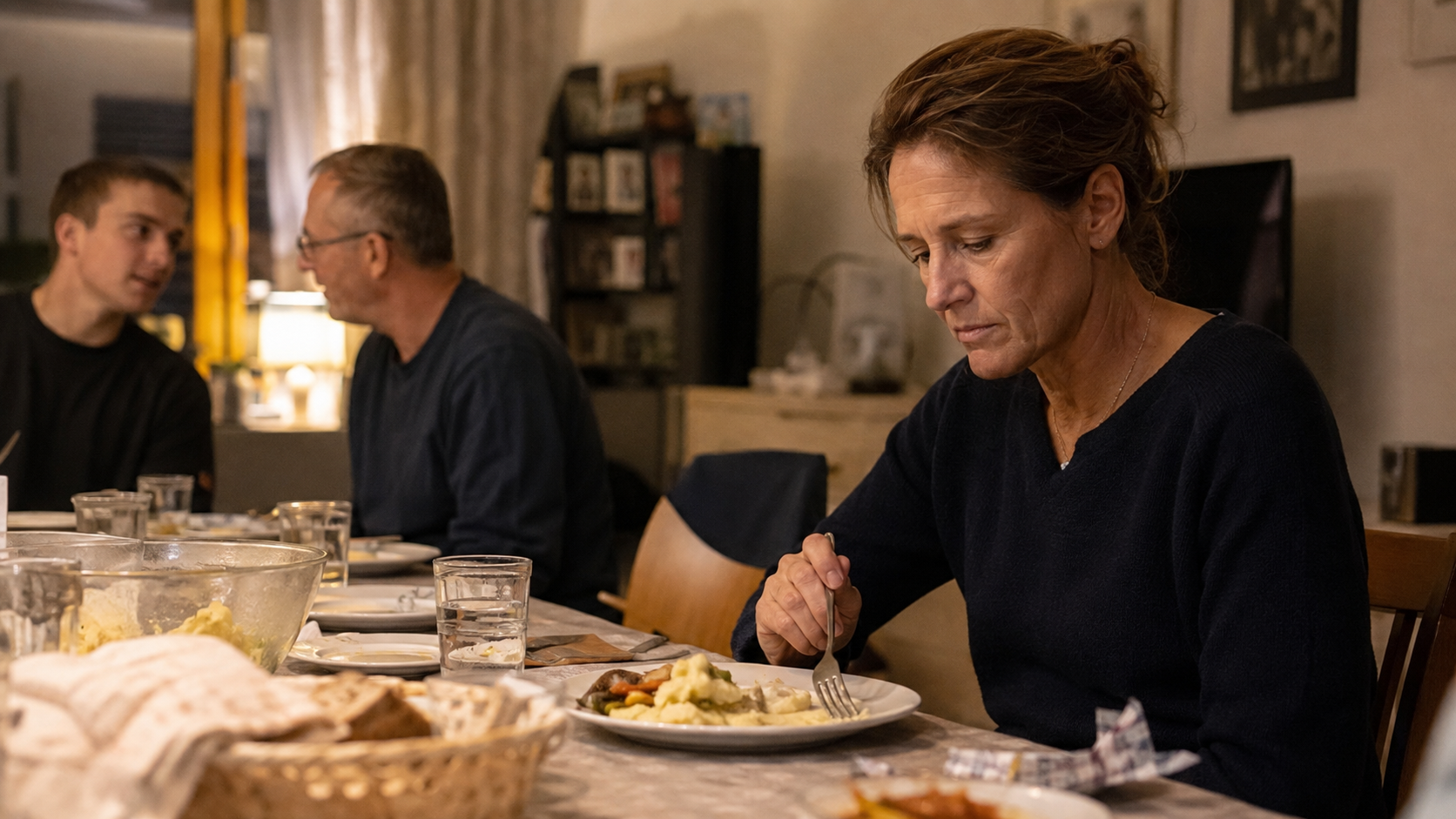 Familienabendessen — jemand sitzt am Tisch, zieht sich innerlich zurück, während die anderen essen; sichtbare Distanz aus Angst vor dem eigenen Blutzucker